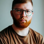 Фронтальный профиль мужчины в очках с рыжей бородой, который смотрит прямо