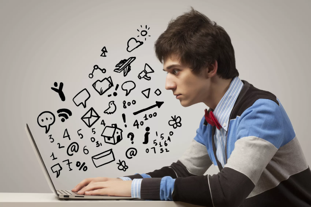 Молодой человек сидит за столом в рубашке, кофте и смотрит в ноутбук с выпученными глазами. Из ноутбука выходят различные знаки и цифры.